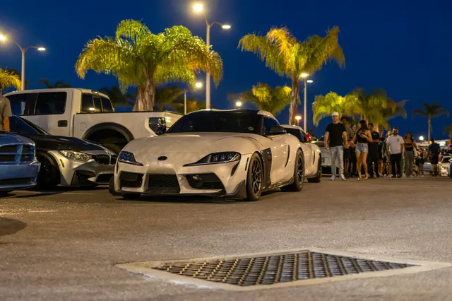 White GR Supra parked among cars under palm trees at night