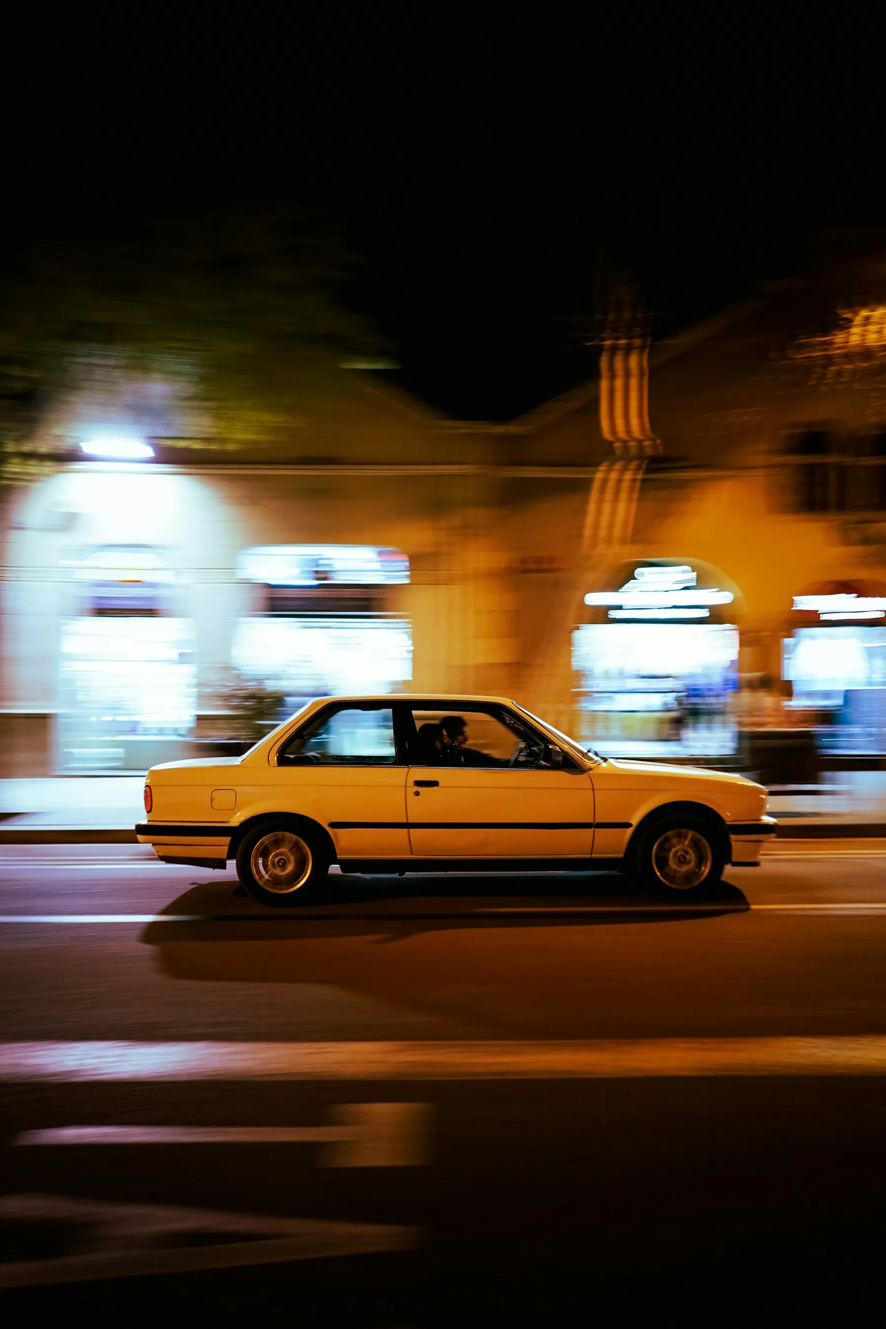 Yellow BMW E30 rolling shot through a lit-up street at night